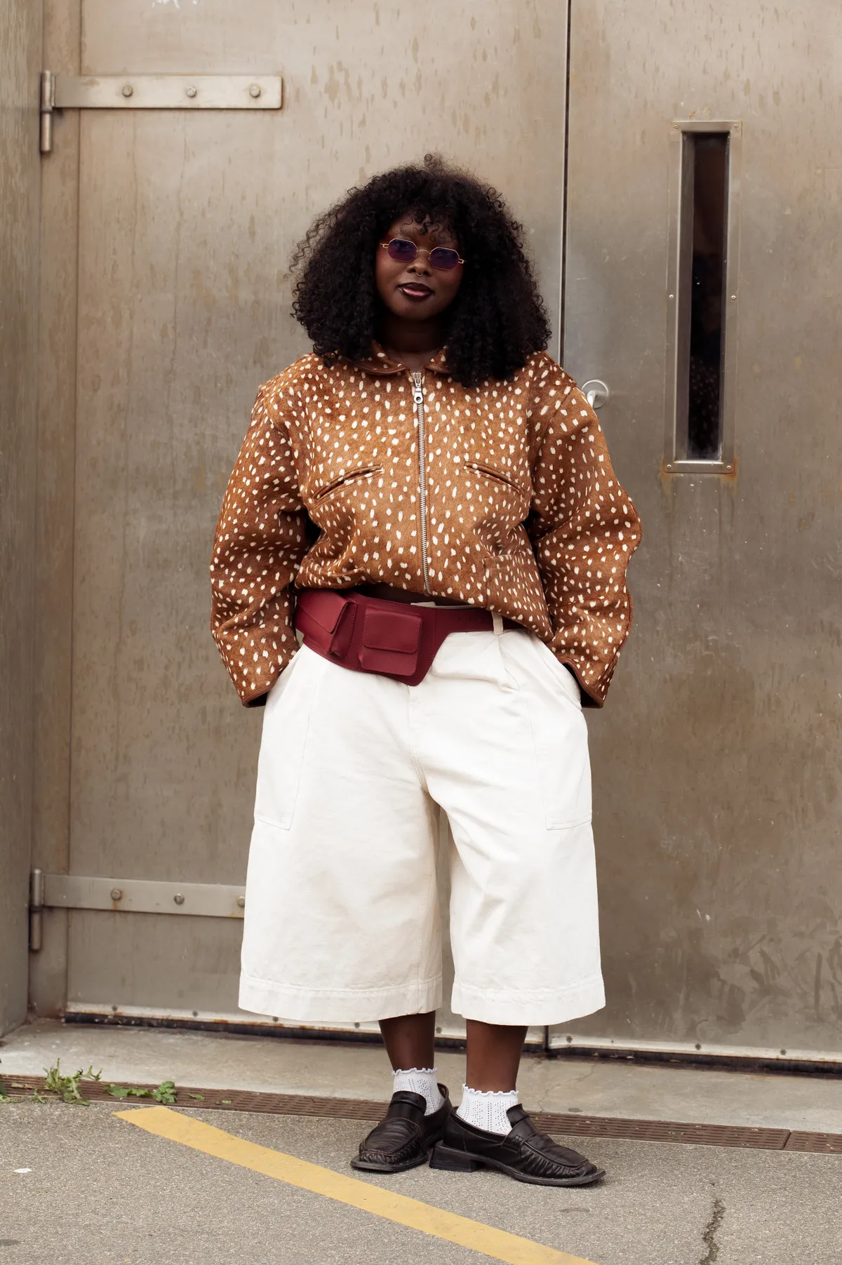 COPENHAGEN, DENMARK - AUGUST 04: A guest wears white wide long shorts, white socks, brown loafers, burgundy belt bag, brown fur jacket with white dots outside Bonnetje show during Copenhagen Fashion Week day one on August 04, 2025 in Copenhagen, Denmark. (Photo by Raimonda Kulikauskiene/Getty Images)