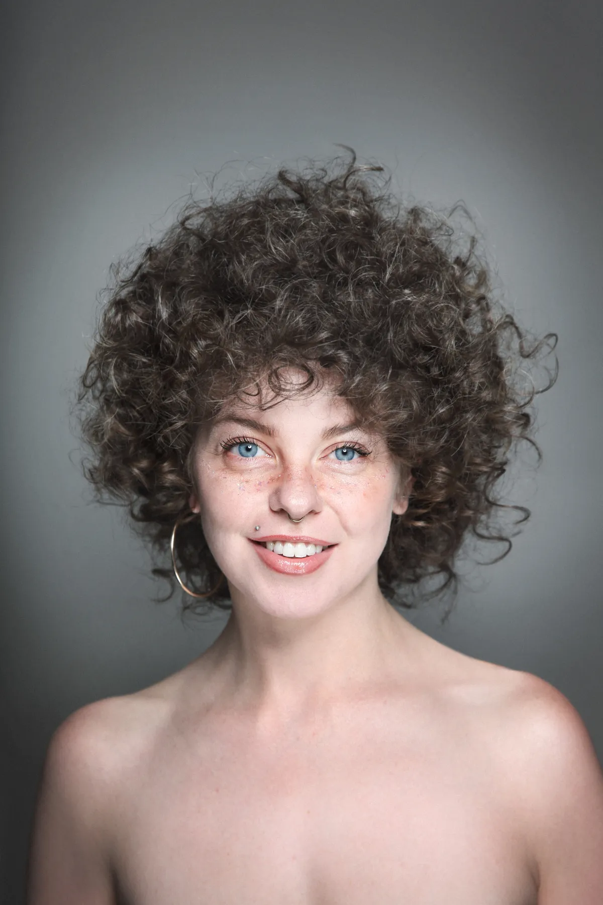 Portrait of young beautiful smiling woman with curly hair, false freckles and piercing