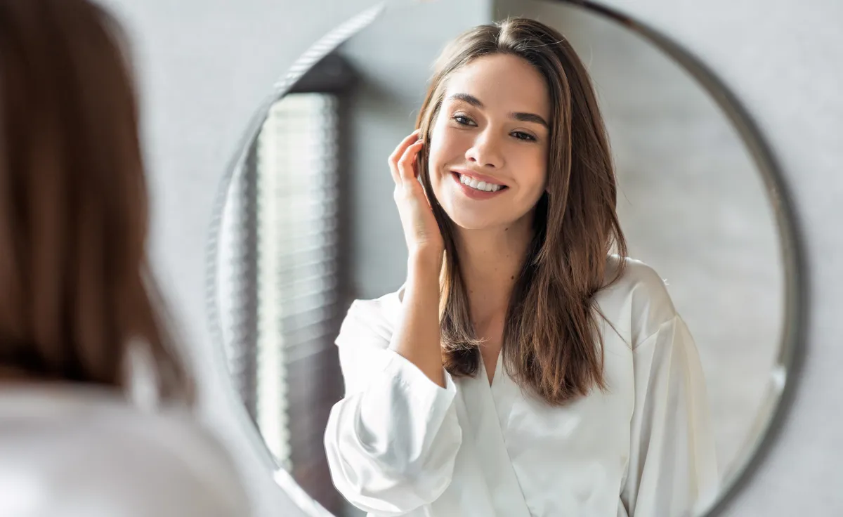 Beauty Concept. Portrait Of Attractive Happy Woman Looking At Mirror In Bathroom, Beautiful Millennial Lady Wearing White Silk Robe Smiling To Reflection, Enjoying Her Appearance, Selective Focus