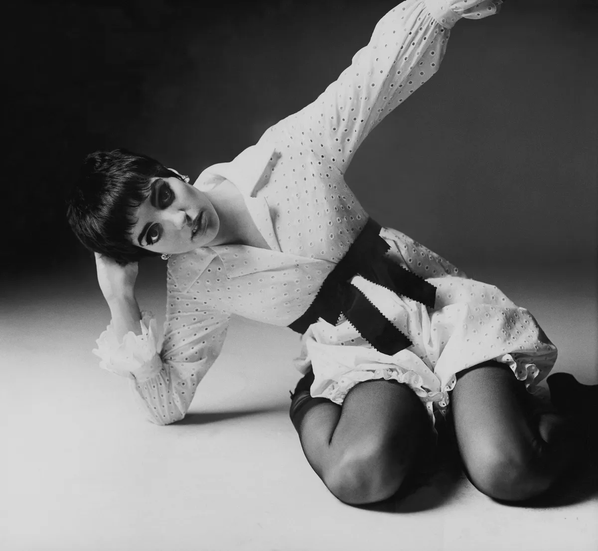 Singer and actress Liza Minnelli kneeling, wearing a bloomer dress of white eyelet, with black ribbon sash at the waist by Youth Guild. (Photo by Bert Stern/Condé Nast via Getty Images)