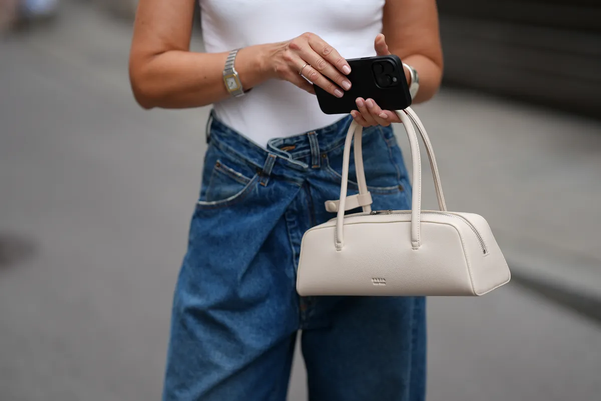 MUNICH, GERMANY - JULY 3: Mirja Klein is seen wearing a bright white MandyMW sleeveless logo top with tight shape and white logo embroidery in the front from MY ESSENTIAL WARDROBE; a blue medium washed Ines denim trousers with fold-over closure and wide leg silhouette from DARKPARK; a white Mercer Bag Oat with elongated shape from Freja; a silver cuff bracelet with sculpted silhouette from COS; a vintage silver-golden bicolor Santos de Cartier wristwatch from Cartier on July 3, 2025 in Munich, Germany. (Photo by Moritz Scholz/Getty Images)