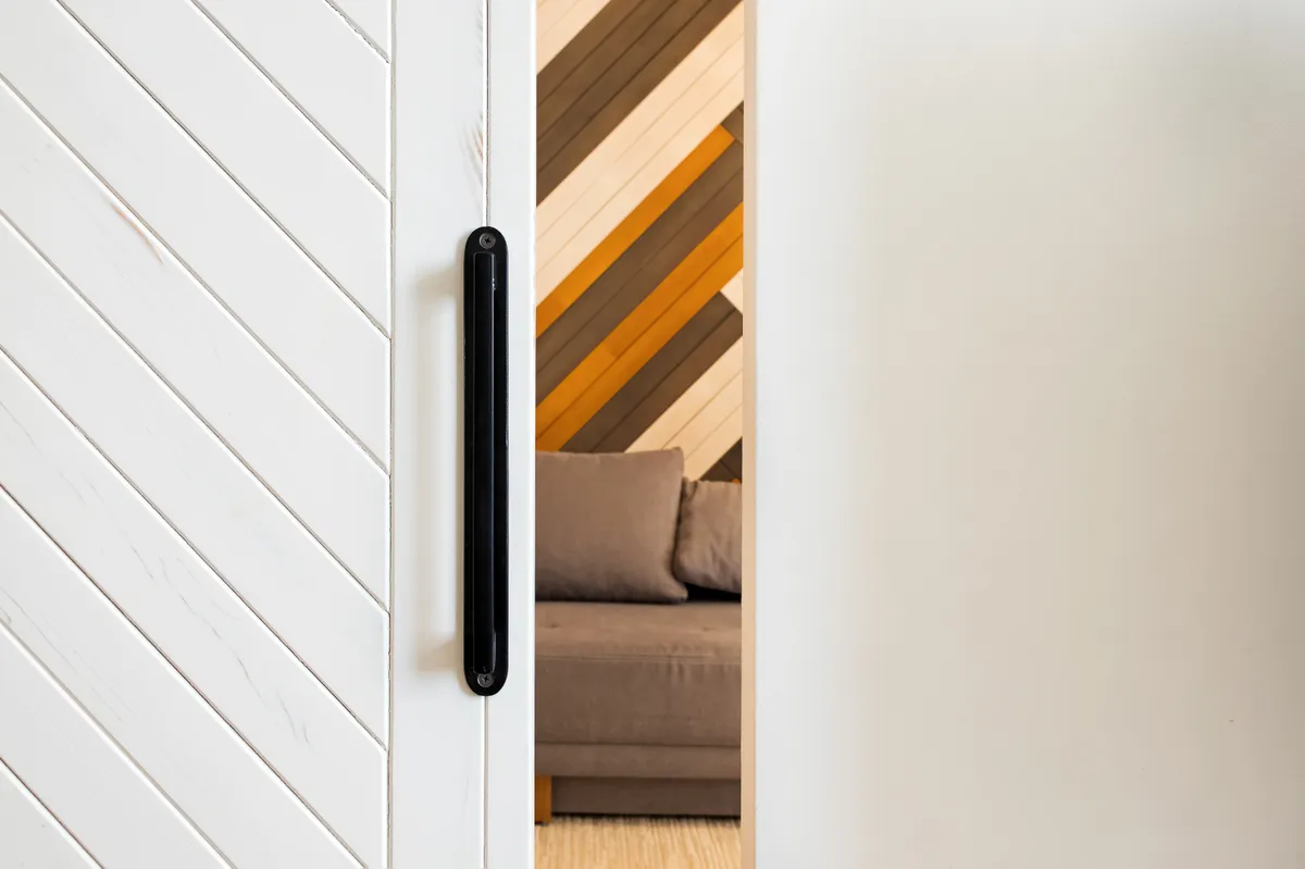 Small gap between white wooden sliding door and wall with room on the background