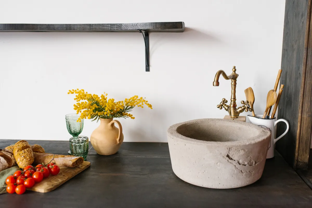 Retro stone sink and mixer golden in the kitchen in the Scandinavian style, a bouquet of mimosa in a clay vase
