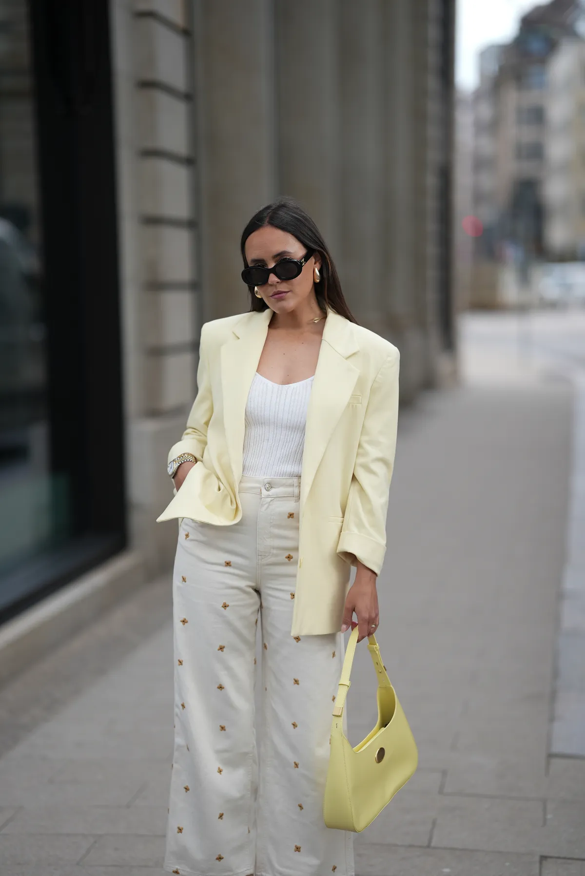 HAMBURG, GERMANY - MAY 5: Laura Noltemeyer is seen wearing a butter yellow blazer from Zara, a knitted v-neck top in viscose crêpe in white from Drykorn, a 5-pocket wide-leg jeans with all-over small flower embroidery in ecru from Sézane x Lucia Vergara, a pale yellow shoulder bag with small golden details from Marc Cain, black TRIOMPHE sunglasses with round glasses and golden logo detail on temples from Celine, golden drop earrings, golden Love bracelets from Cartier, stacked rings from Cartier, small silver-golden Datejust watch from Rolex on May 5, 2025 in Hamburg, Germany. (Photo by Moritz Scholz/Getty Images)