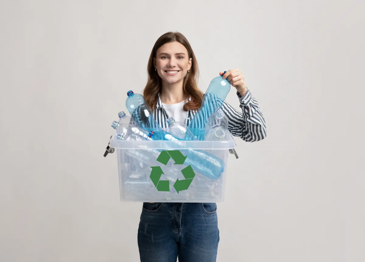 Waste For Recycling. Cheerful Young Woman Carrying Container Box With Empty Plastic Bottles, Positive Millennial Female Sorting Garbage, Enjoying Zero Waste Living, Standing On Grey Studio Background