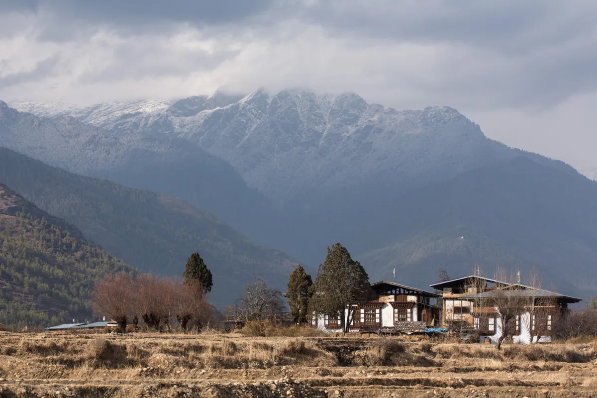 Farmhouses in the Paro Valley with a snow-capped mountain shrouded with clouds in the background. (Photo by: Jon G. Fuller/VW Pics /Universal Images Group via Getty Images)