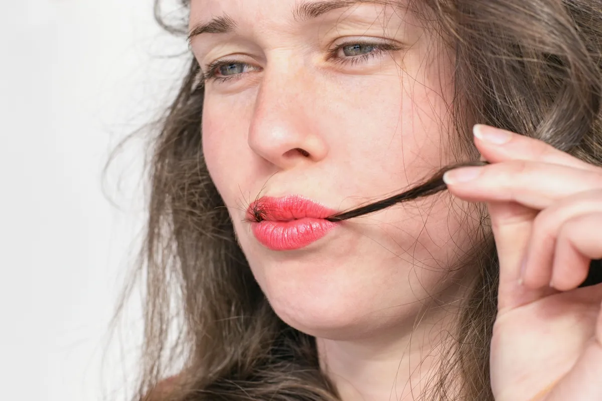 A hajevés segélykiáltás: a test üzenete arról, hogy a lélek nincs rendben. Young beautiful woman with hair strand in red lips. Trichophagia - compulsive eating of hair associated with trichotillomania (hair pulling)