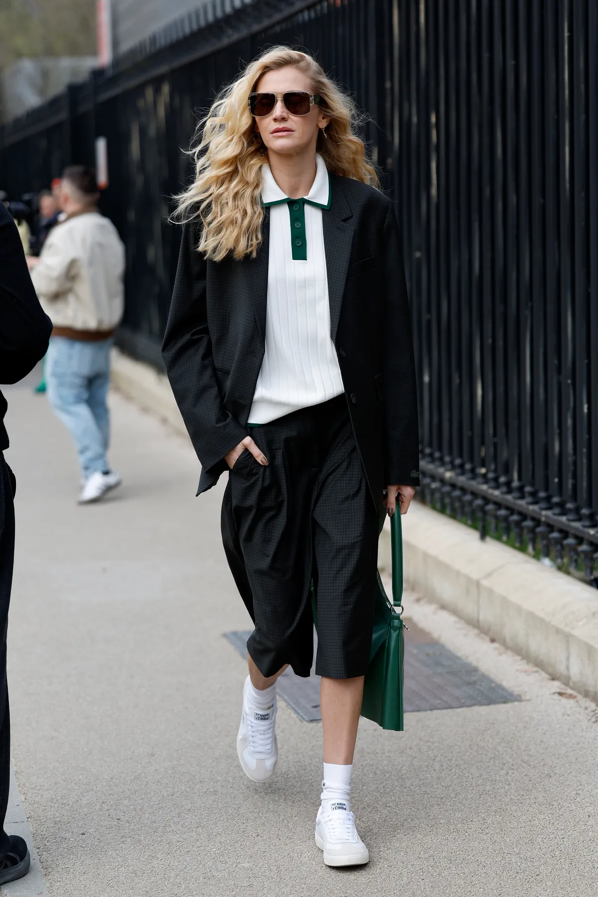PARIS, FRANCE - MARCH 09: Celina Locks wears white polo neck top with green detail, black Lacoste blazer with matching bermuda shorts, green Lacoste bag, white socks, white Lacoste sneakers, outside Lacoste, during the Womenswear Fall/Winter 2025/2026 as part of Paris Fashion Week on March 09, 2025 in Paris, France. (Photo by Claudio Lavenia/Getty Images)