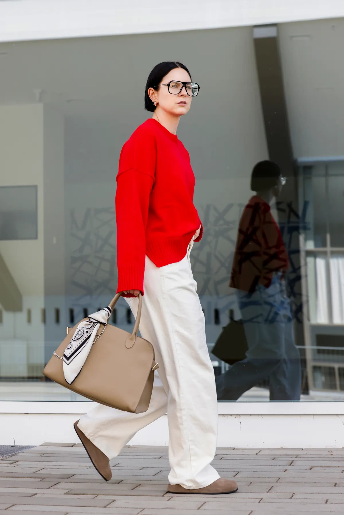 ESSEN, GERMANY - SEPTEMBER 15: Art director Maria Barteczko, wearing a red oversize wool sweater by Cos, ecru white wide leg jeans by Source Unknown, beige suede Hugo clog slides by The Row, a beige margaux leather tote bag with chain and scarf around by the Row and black oversize Aviator eyewear glasses by Victoria Beckham, during a streetstyle shooting on September 15, 2024 in Essen, Germany.  (Photo by Streetstyleshooters/Getty Images)