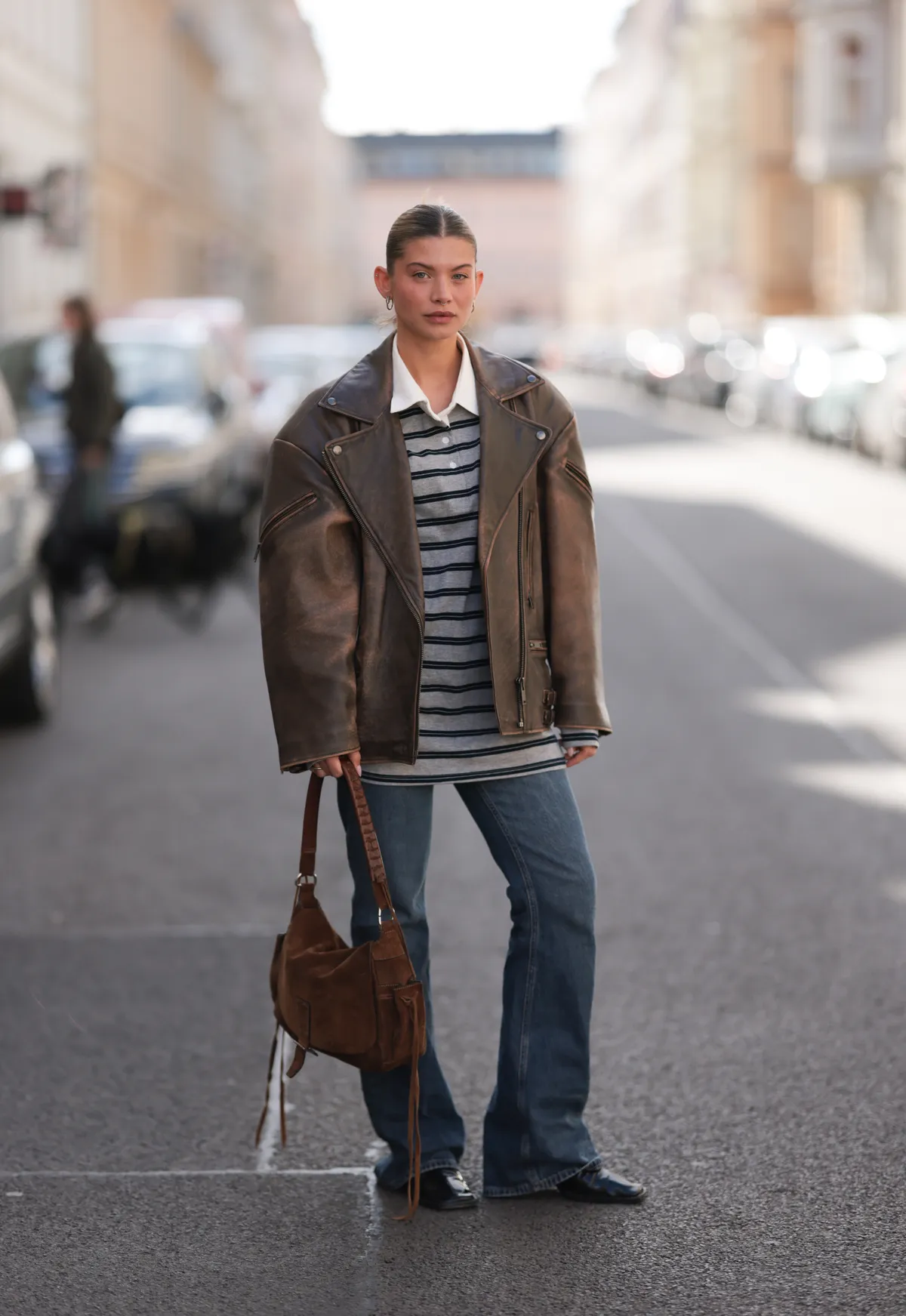 BERLIN, GERMANY - APRIL 08: Sophia Geiss seen wearing minimal hoop earrings, The Frankie Shop grey and navy striped rugby shirt featuring a crisp white polo collar, Ducie London oversized brown leather jacket with a slightly distressed, vintage finish, adding a rugged and effortlessly cool vibe to the outfit, Mango classic bootcut jeans in a medium blue wash, medium-sized brown suede vintage shoulder bag with braided leather straps and long fringe detailing and Jil Sander black, pointed leather boots, on April 08, 2025 in Berlin, Germany. (Photo by Jeremy Moeller/Getty Images)