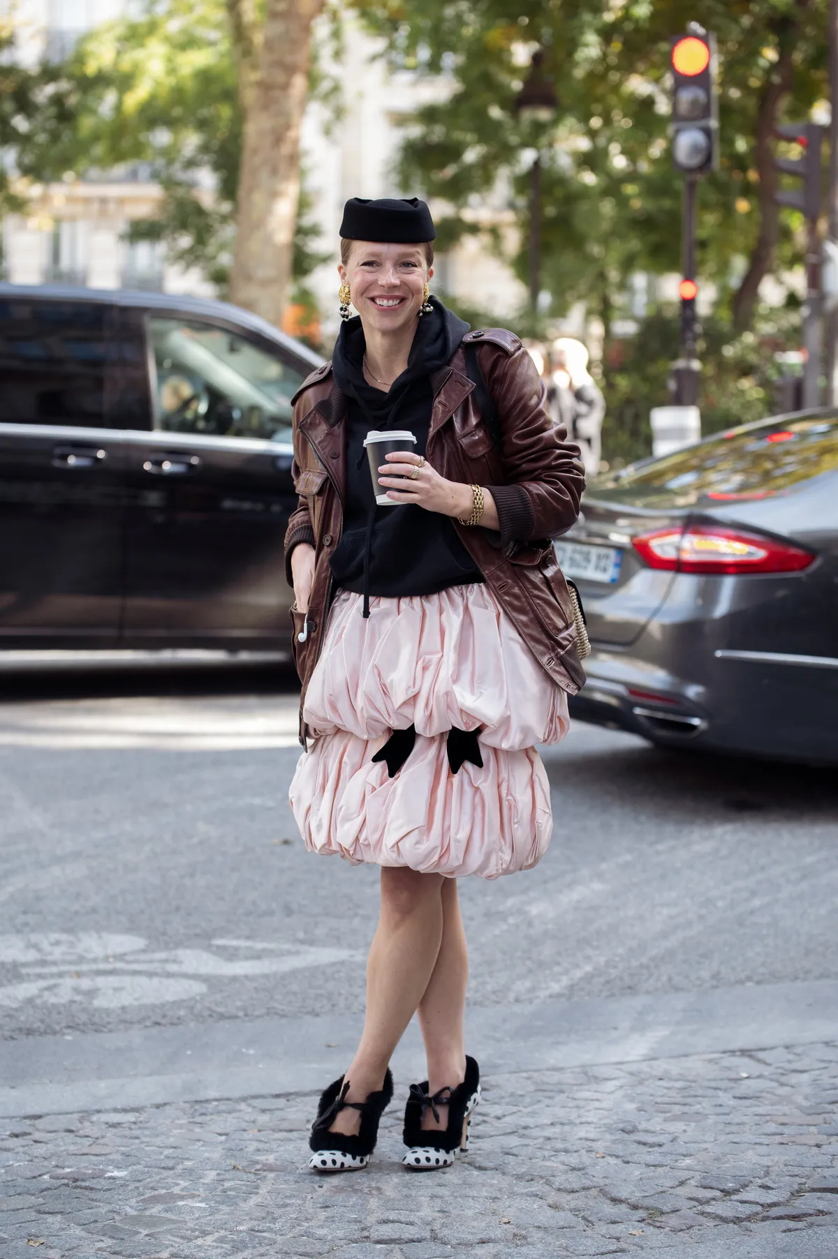 PARIS, FRANCE - OCTOBER 02: Chloe King wears a brown leather jacket over a black hoodie and a voluminous pink satin bubble skirt, paired with polka dot fur-trimmed heels, a black hat, and gold jewellery outside Mugler show during the Womenswear Spring Summer 2026 as part of Paris Fashion Week on October 02, 2025 in Paris, France. (Photo by Raimonda Kulikauskiene/Getty Images)