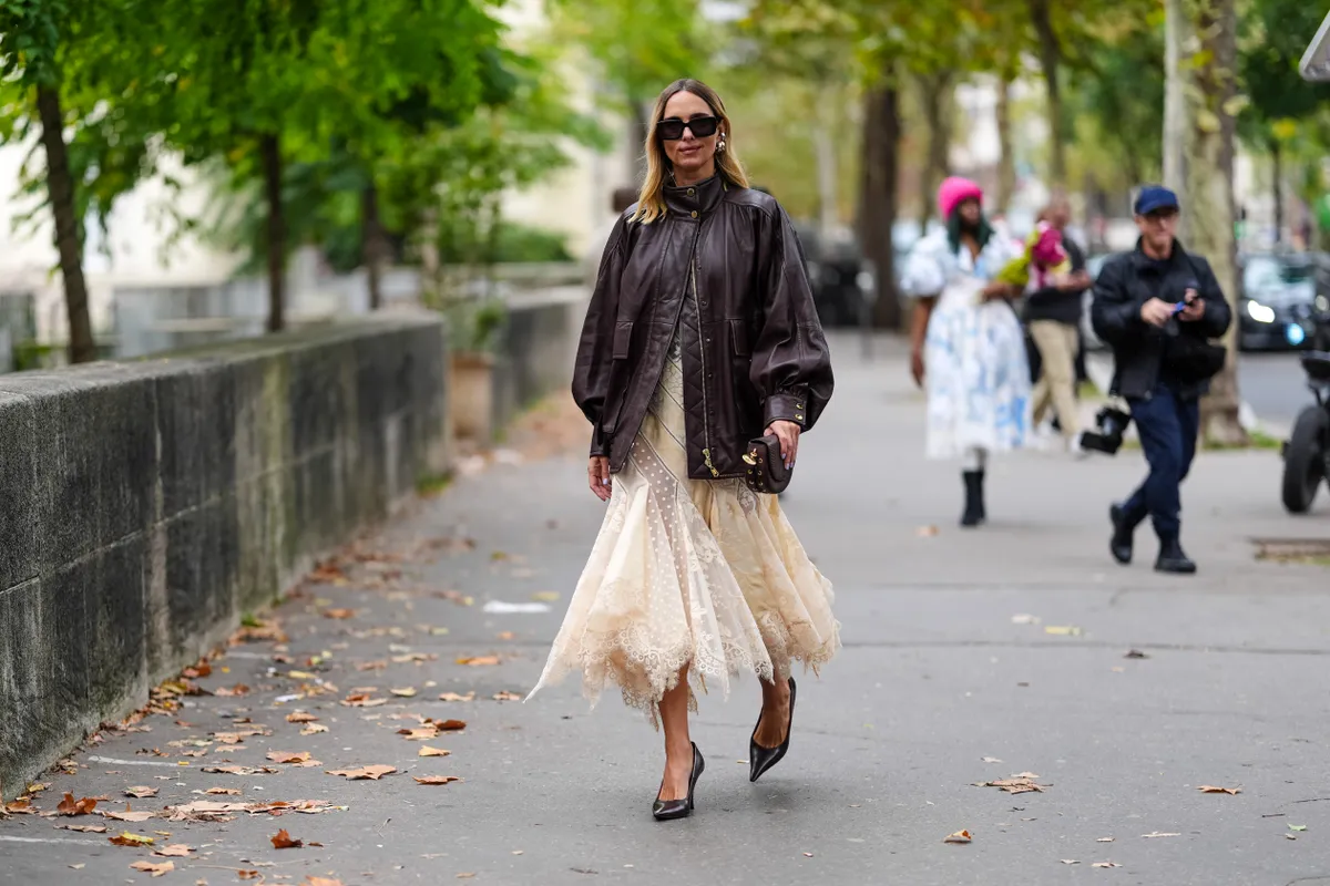 PARIS, FRANCE - SEPTEMBER 30: Candela Novembre wears black sunglasses, gold earrings, shiny dark brown oversized bomber leather jacket, cream sheer mesh mermaid flared midi skirt, shiny black pointed toe leather kitten heels, dark brown leather bag, outside Zimmermann, during the Paris Fashion Week Spring/Summer 2025 on September 30, 2024 in Paris, France (Photo by Edward Berthelot/Getty Images)