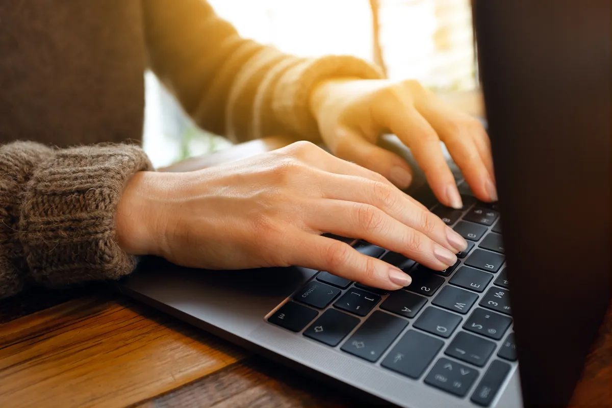 Egy nő a laptopján munkahelyi e-mailt ír a billentyűzet segítségével.