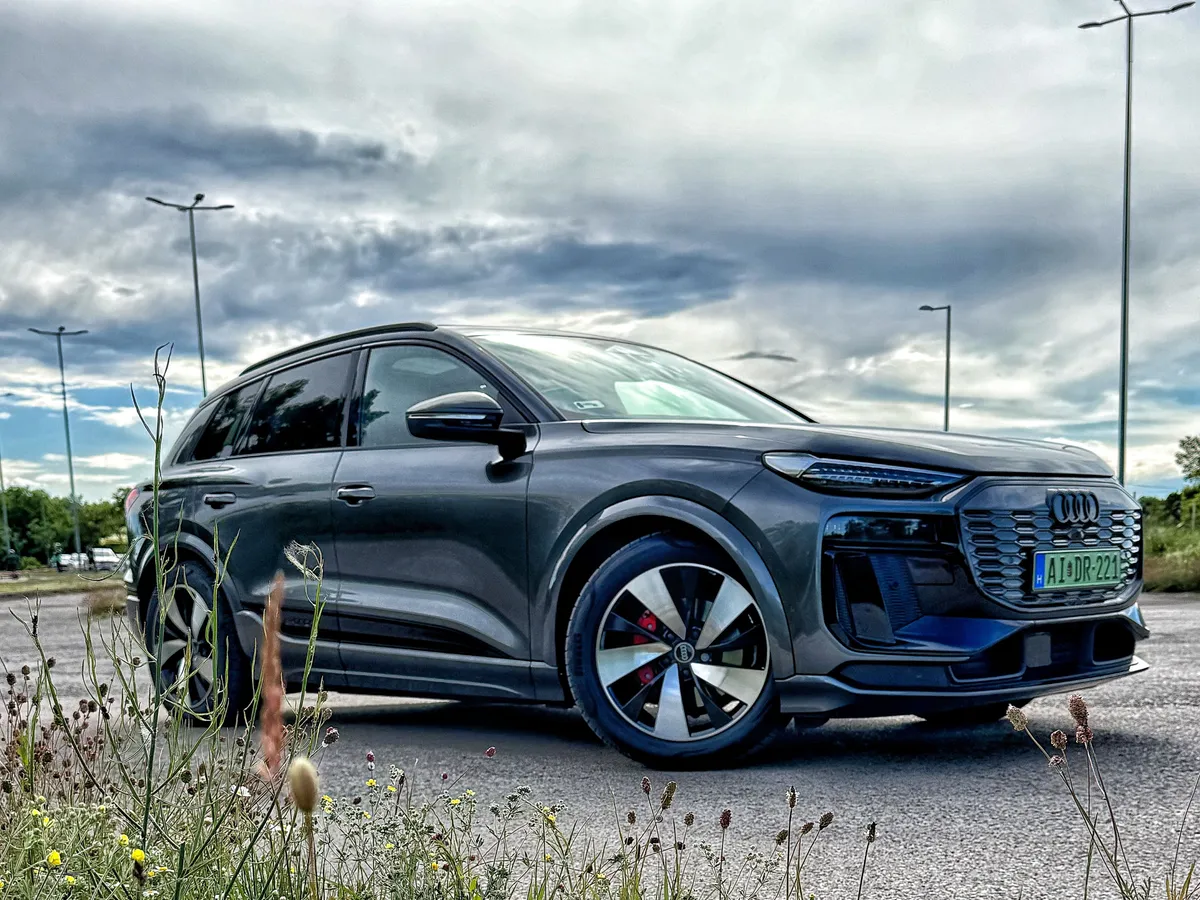 Audi Q6 modell oldalról fotózva egy parkolóban.