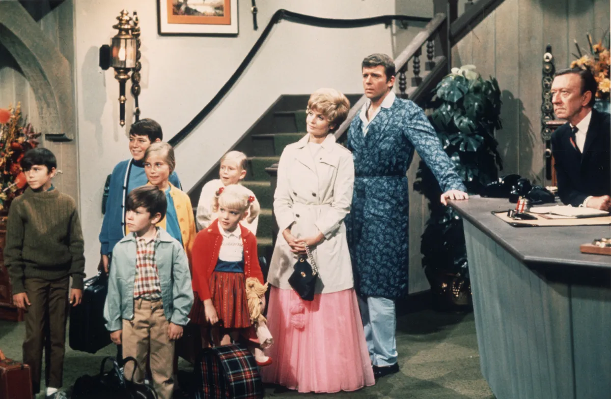 American actors Robert Reed and Florence Henderson stand in a hotel lobby with their television family in a still from the TV series 'The Brady Bunch,' circa 1969. (L-R) Christopher Knight, Barry Williams, Mike Lookinland, Maureen McCormick, Eve Plumb, Susan Olsen, Henderson, Reed, unidentified. (Photo by Paramount Television/Courtesy of Getty Images)