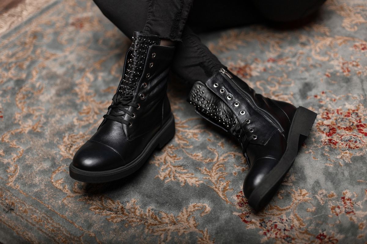 Fashionable young woman is sitting on a vintage floor in a store in black stylish leather shoes with lacing in jeans. Close up of female legs in trendy autumn spring boots. New stylish shoe collection