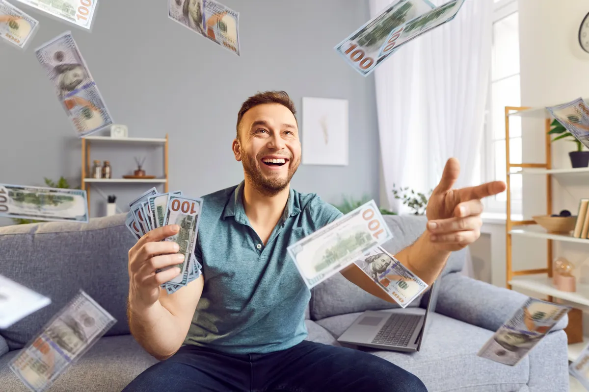 Sokat küzdött mosatanában 6 csillagjegy, de végre érkezik hozzájuk a szerencse, a bőség. Happy and rich man making money rain with dollar banknotes, celebrating financial success or win at home. Prosperity and financial abundance, illustrating cash wealth, success, and luxury.