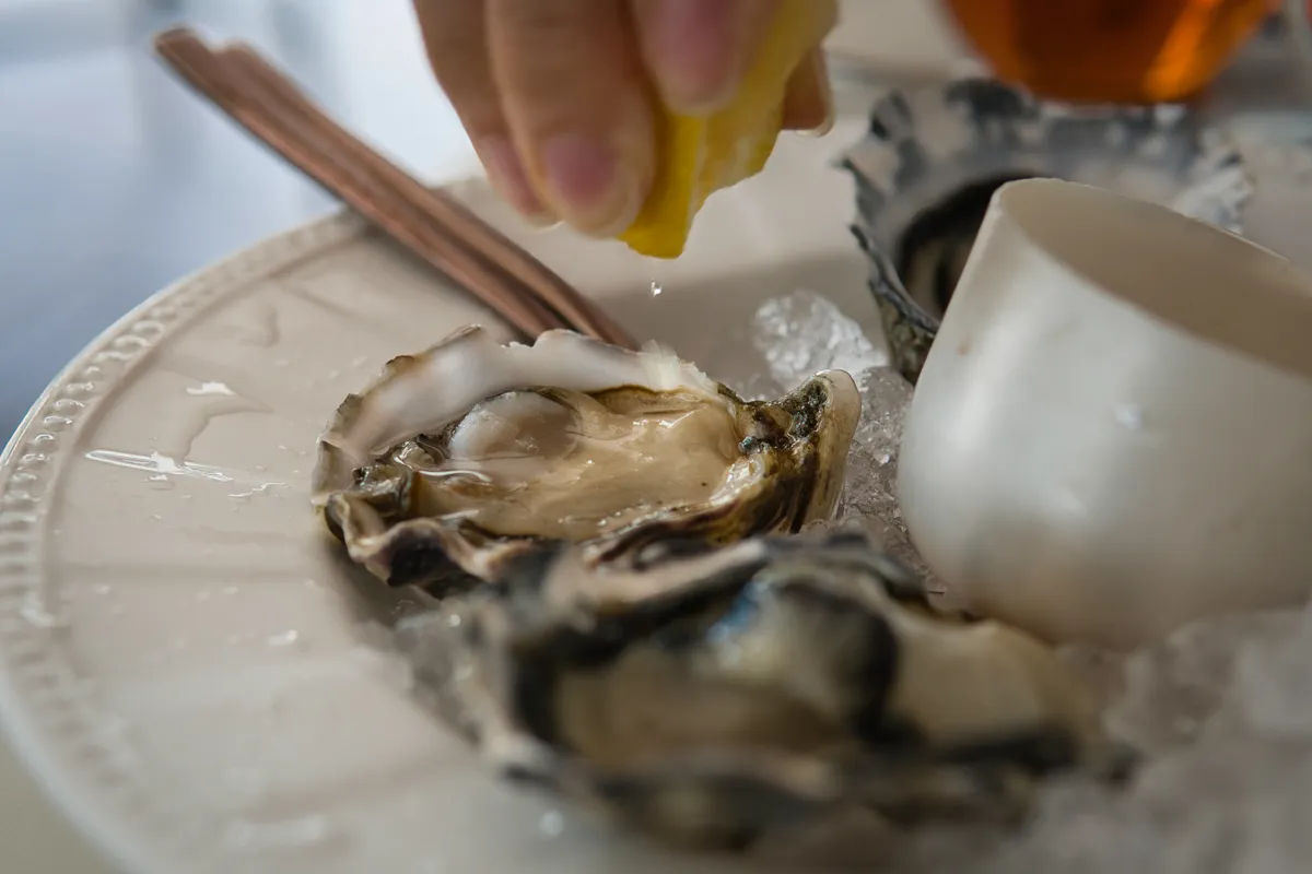 Hand,Squeezing,Lemon,Juice,Onto,Fresh,Oysters,On,White,Plate
osztriga
