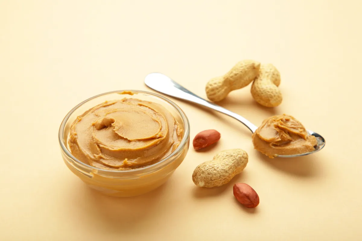 Bowl of peanut butter and peanuts on beige background. Creamy peanut pasta in small bowl. mogyoróvaj