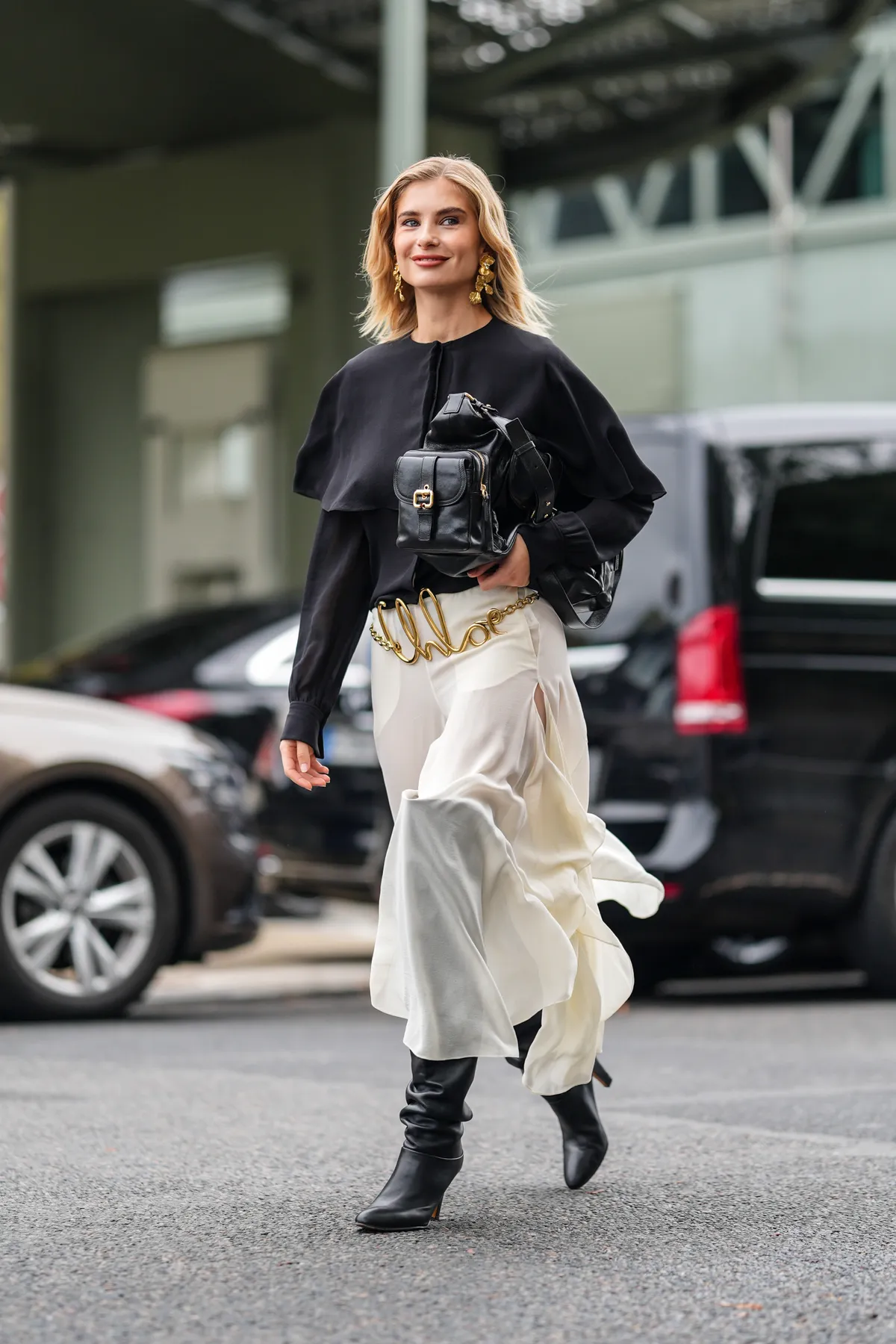 PARIS, FRANCE - SEPTEMBER 26: Xenia Adonts wears black long sleeve shirt, shiny black Chloe leather bag, gold Chloe belt, white sheer mesh flowy asymmetrical Chloe midi skirt, shiny black thigh high heeled leather boots, outside Chloe, during the Paris Fashion Week Spring/Summer 2025 on September 26, 2024 in Paris, France (Photo by Edward Berthelot/Getty Images)