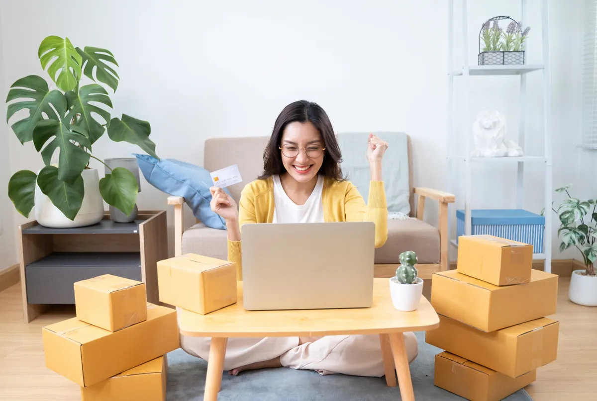 Egy nő online vásárlás után a hitelkártyájával a kezében a laptopja előtt. 