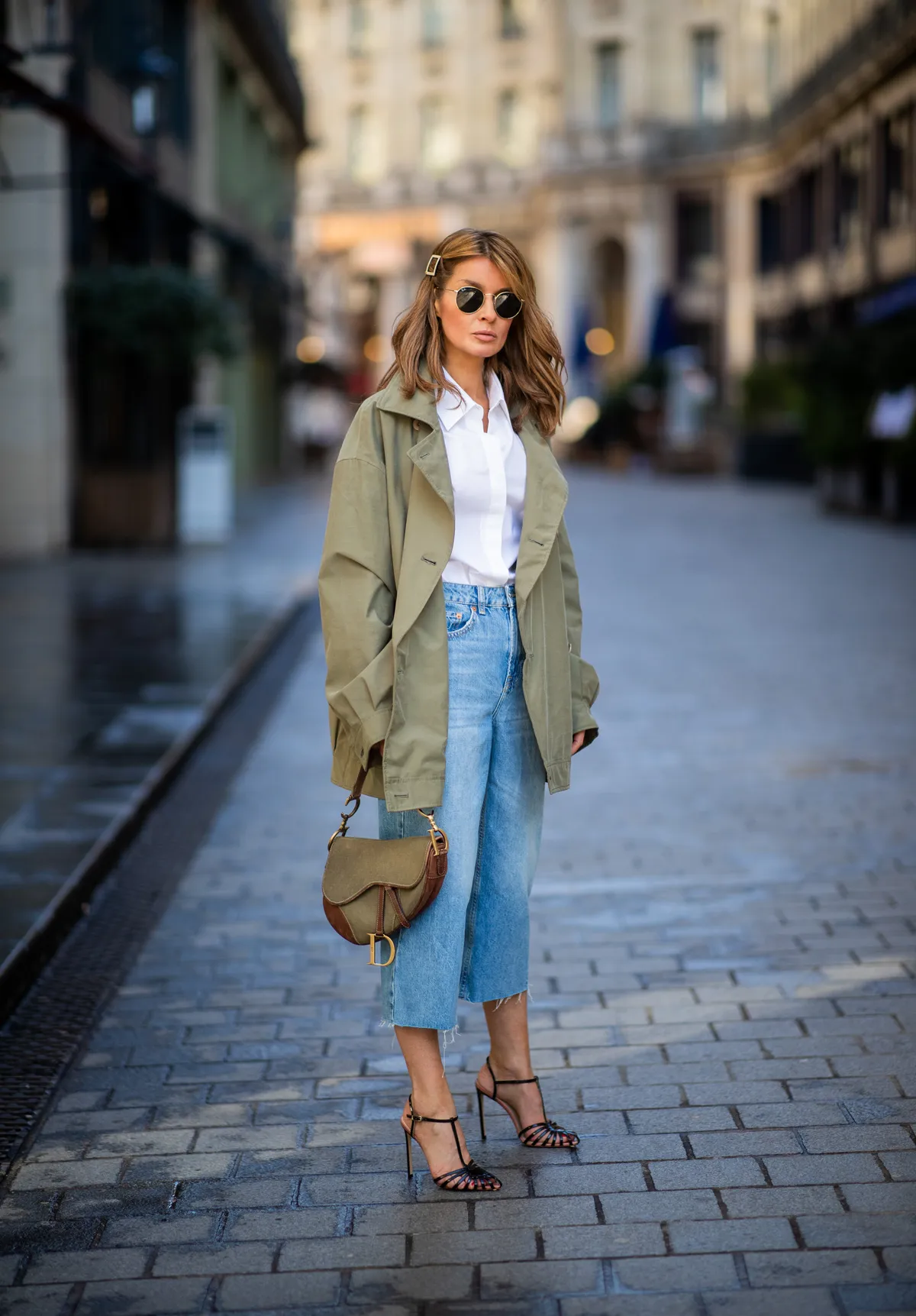 PARIS, FRANCE - FEBRUARY 26: Gitta Banko is seen wearing a white blouse with puffy sleeves and flounces by Balossa, khaki-colored utility style parka by glab, bleach slime wide legs jeans from Topshop, khaki canvas Saddle Bag by Dior, black naked strap sandals by Francesco Russo and gold round metal sunglasses by Ray Ban during Paris Fashion Week Womenswear Fall/Winter 2019/2020 on February 26, 2019 in Paris, France. (Photo by Christian Vierig/Getty Images)