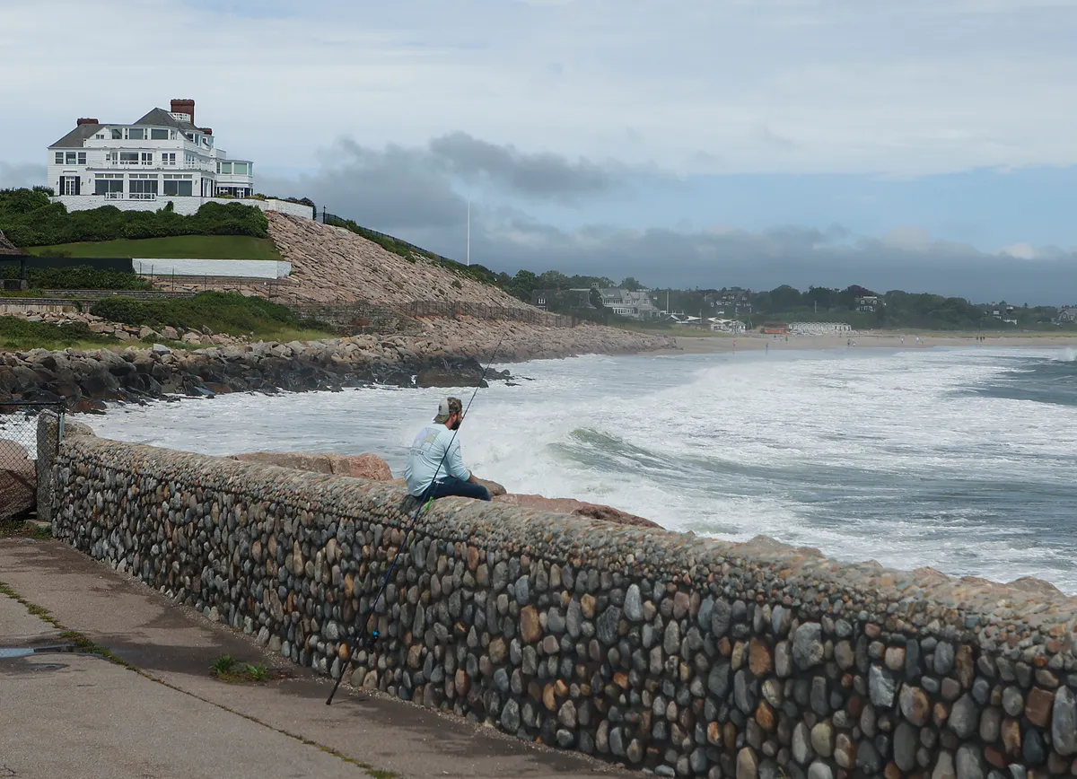 Westerly, RI - August 22: A man fishes at the Watch Hill Lighthouse for stripped bass with home of Taylor Swift in the background during the eye of the Tropical Storm Henri in Westerly, RI on Aug. 22, 2021. (Photo by Matthew J. Lee/The Boston Globe via Getty Images)