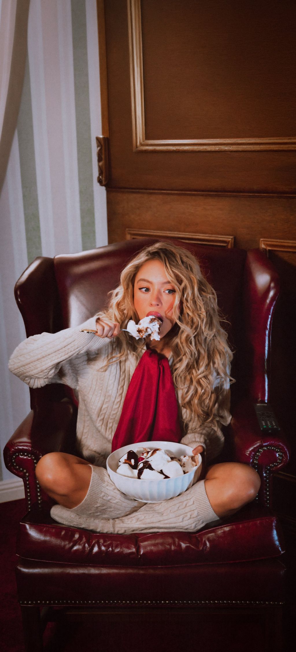 Sydney Sweeney szexi, kötött pulóverben és piros kendőben, fagylaltot majszolva hozza el a Reszkessetek, betörők! hangulatát. 
