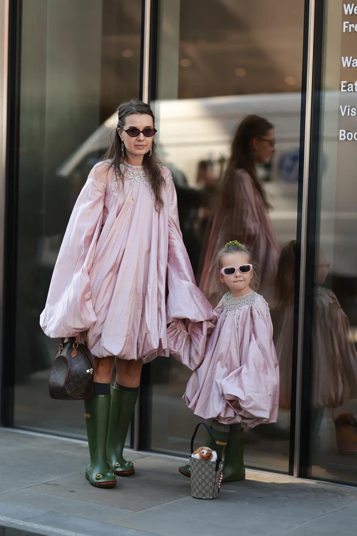 LONDON, ENGLAND - SEPTEMBER 19: A brown-haired Guest is seen wearing a rose puffer dress, green rubber boots with frog face and a Louis Vuitton leather handbag, sunglasses and silver earrings and her daughter seen wearing the matchy outfit, rose puffer dress, green rubber boots with frog face, rose sunglasses, a green hairband and a Gucci bag with stuffed animal outside MITHRIDATE Show during London Fashion Week on September 19, 2025 in London, England. (Photo by Jeremy Moeller/Getty Images)