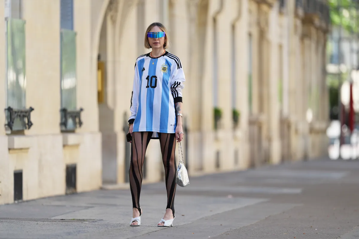 PARIS, FRANCE - APRIL 13: Emy Venturini wears sunglasses from Pierre Cardin, a Cartier watch, a blue and white striped Argentina soccer t-shirt from Adidas with printed "10" on the front and "Messi" on the back, black mesh striped stirrup leggings from Mugler, a silver bag from Rabanne, kitten heels white leather Balenciaga shoes, during a street style fashion photo session, on April 13, 2024 in Paris, France. (Photo by Edward Berthelot/Getty Images)
