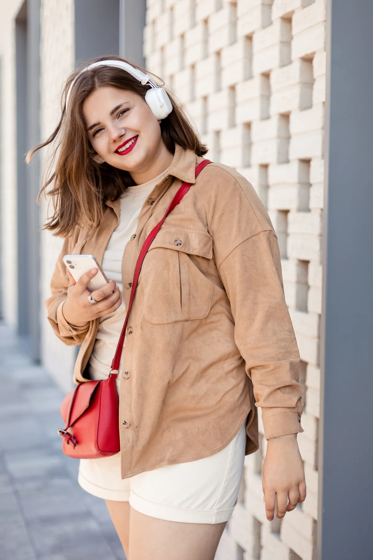 Portrait of young plus size woman on the terrace. listening to music from phone in big headphones. and smiles and looks into the camera. Leisure concept.