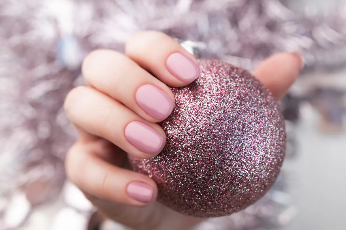 Hand with pink glitter Christmas ball and pink gel fingernails
