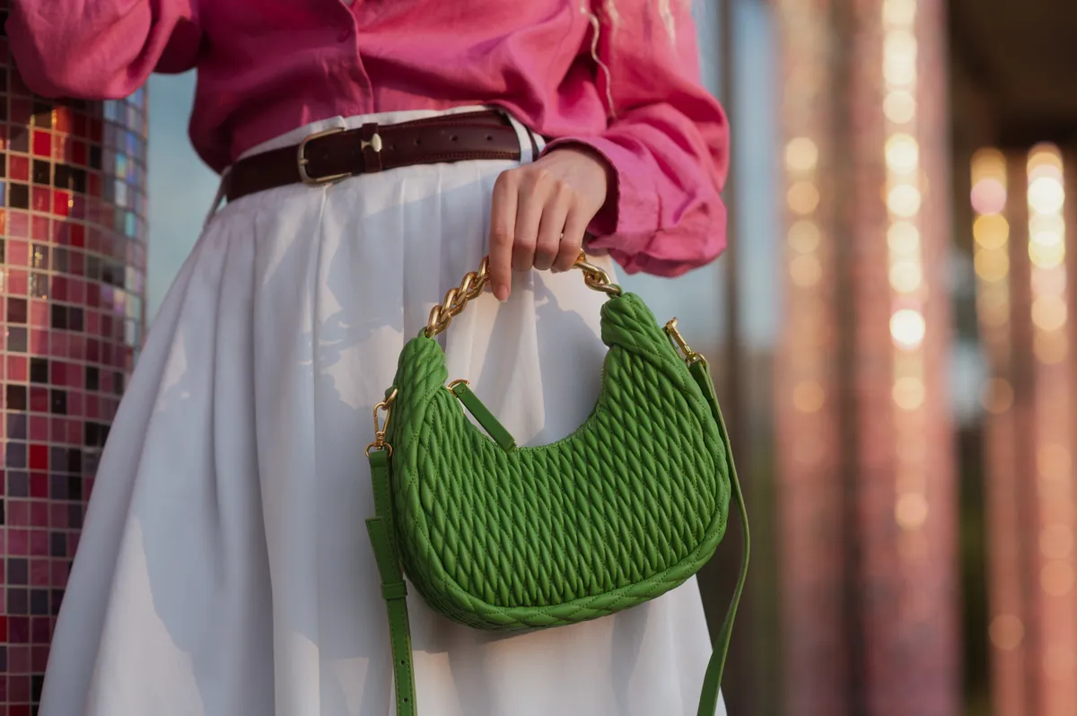 Street fashion details: woman wearing trendy summer outfit, carrying green color quilted faux leather bag. Copy, empty space for text