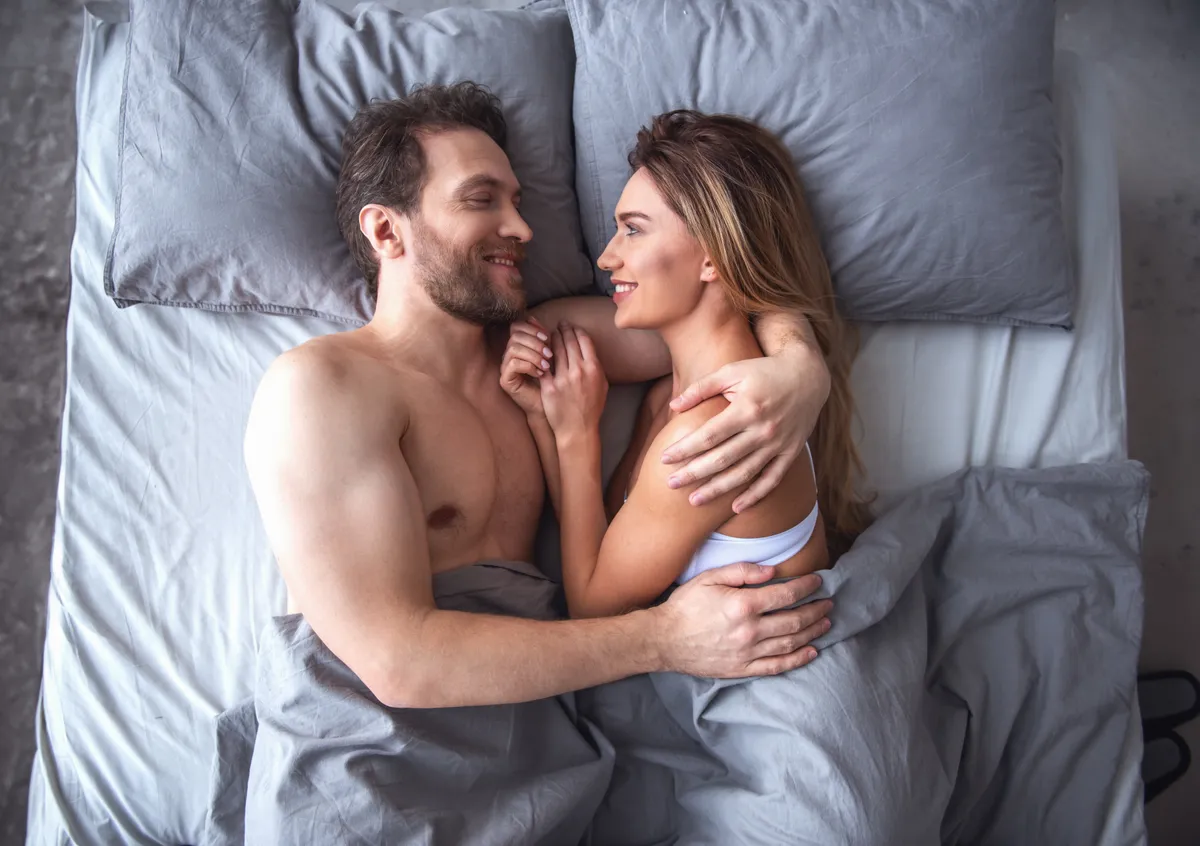Top view of beautiful couple hugging and smiling while lying together in bed at home