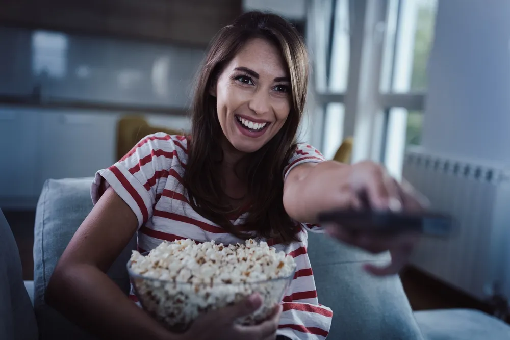 Nő távkapcsolóval és pop cornnal, szívtiprók a TV-ben. 