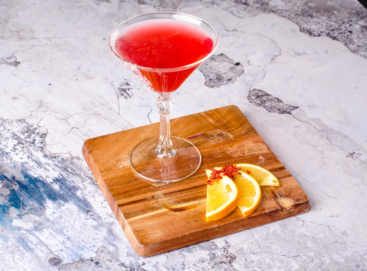 Top view red orange cocktail Cosmopolitan fresh in a martini glass on a wooden board, gray background. Bar alcohol drink menu, delicious tequila sunrise long drink.