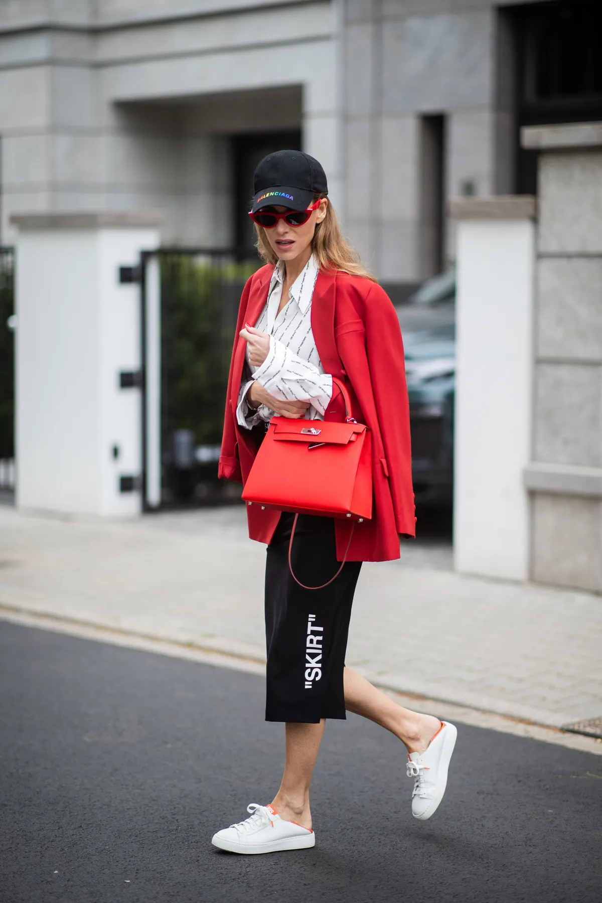 DUESSELDORF, GERMANY - MAY 01: Alexandra Lapp is seen wearing a black logo pencil skirt from OFF-WHITE, a white shirt with a pinstripe quote from OFF-WHITE, a red long Blazer from Valentino, a red Hermes Kelly bag, a black base cap with the logo print in rainbow colors from Balenciaga and limited Santoni sneakers in white and orange with an open heel on May 01, 2019 in Duesseldorf, Germany.