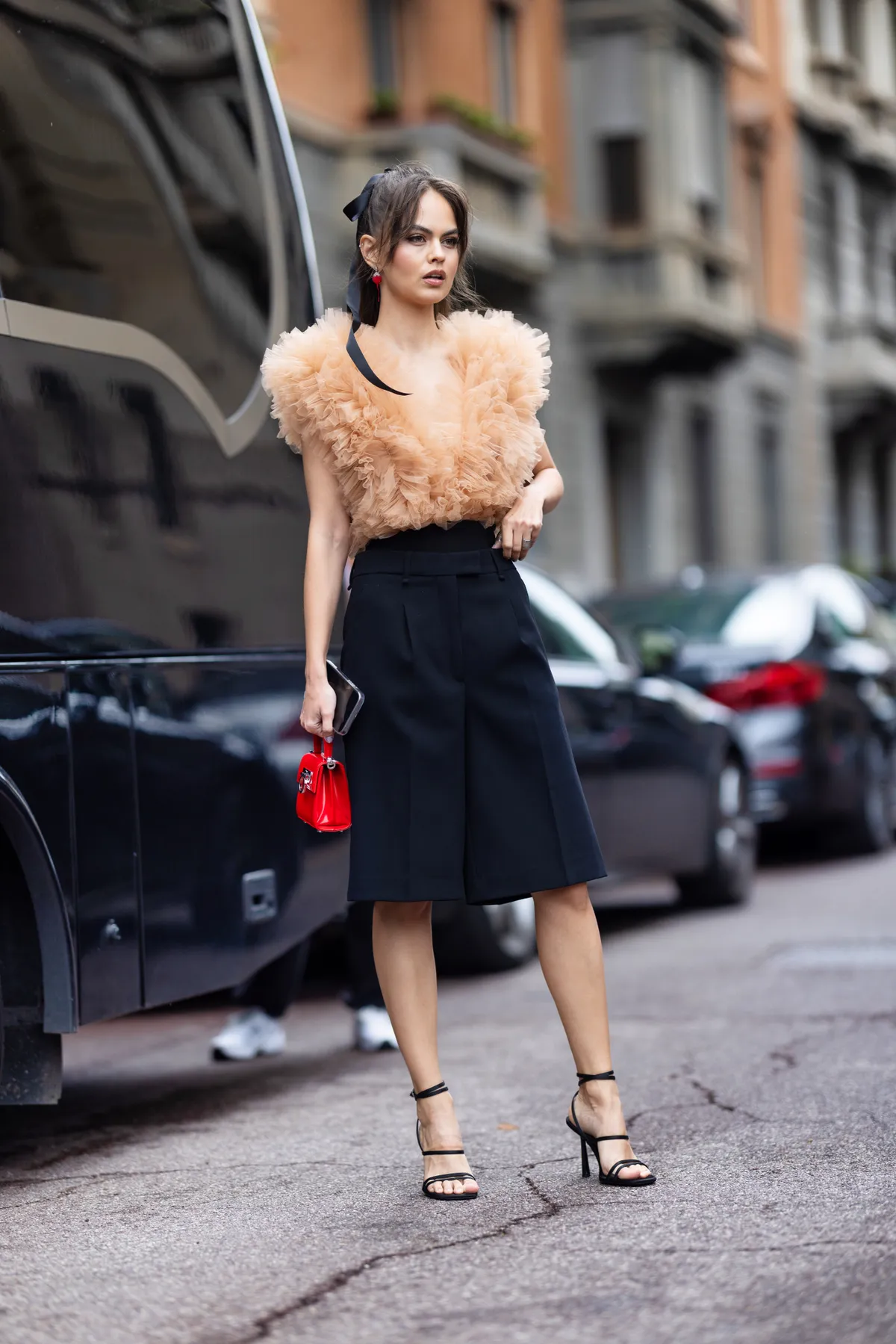 MILAN, ITALY - SEPTEMBER 22: A guest is seen wearing a black bow in the hair, black heels, a red Ferragamo bag, a salmon pink top with rouches and black bermuda shorts, outside the Philosophy show during the Milan Fashion Week - Womenswear Spring/Summer 2024 on September 22, 2023 in Milan, Italy. (Photo by Valentina Frugiuele/Getty Images)
