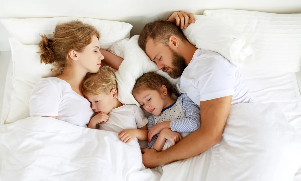 Házasságban élő pár a gyerekeivel egy fehér ágyban alszik