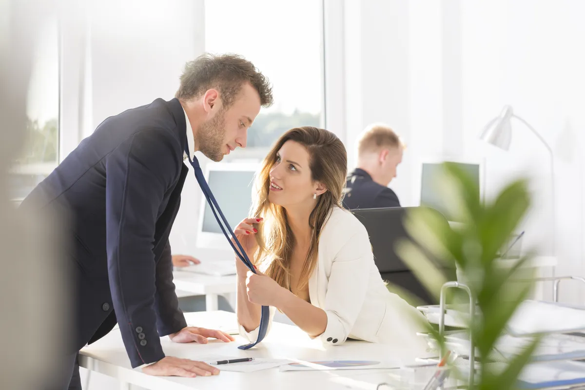 Woman grabbing man's tie and flirting at work
