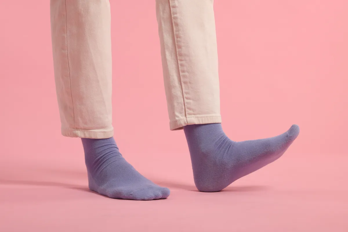 Woman in stylish purple socks and pants on pink background, closeup