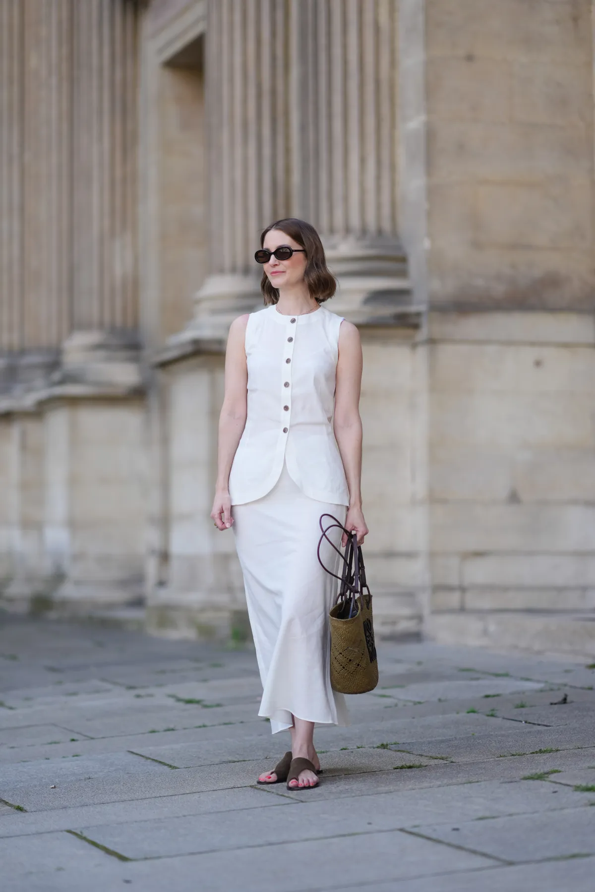 PARIS, FRANCE - MAY 25: Marissa Cox wears a white Arket linen skirt set, a sleeveless long top with buttons, a brown raffia Loewe basket bag, ATP Atelier brown suede sandals / shoes, Jimmy Fairly x Reformation sunglasses, during a street style fashion photo session, on May 25, 2024 in Paris, France. (Photo by Edward Berthelot/Getty Images)